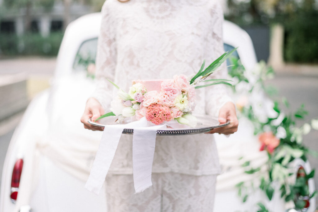 bride holding a mini cake Bride in a lace pants suit holding a pink floral mini cake during micro wedding in Charleston