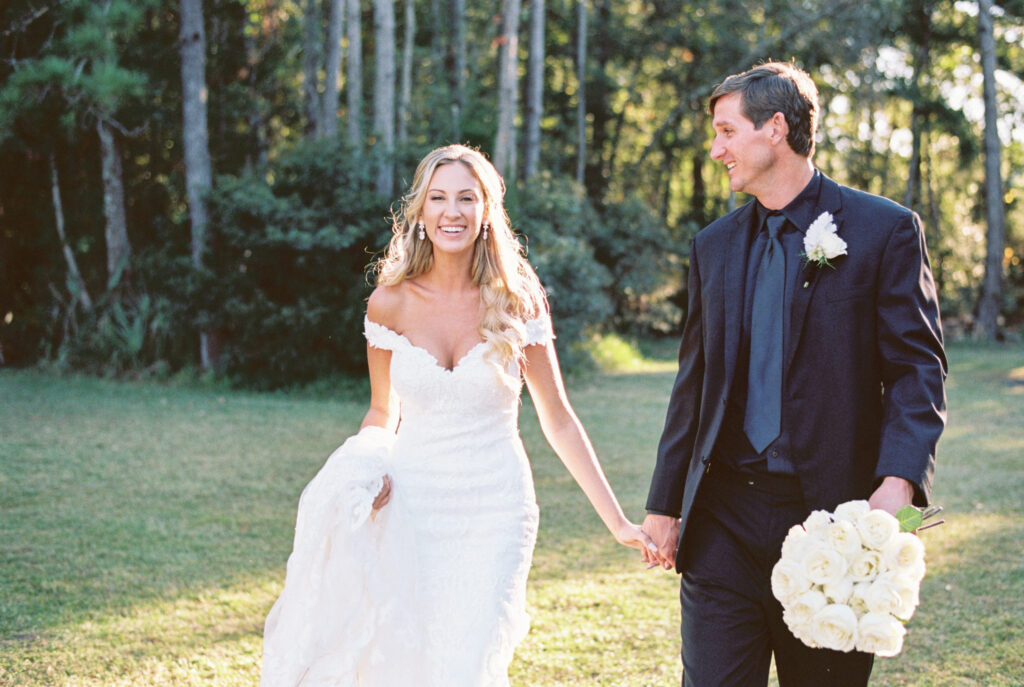 Bride and groom at sunset with white roses Bride and groom walking holding hands with white long stem rose bouquet at sunset