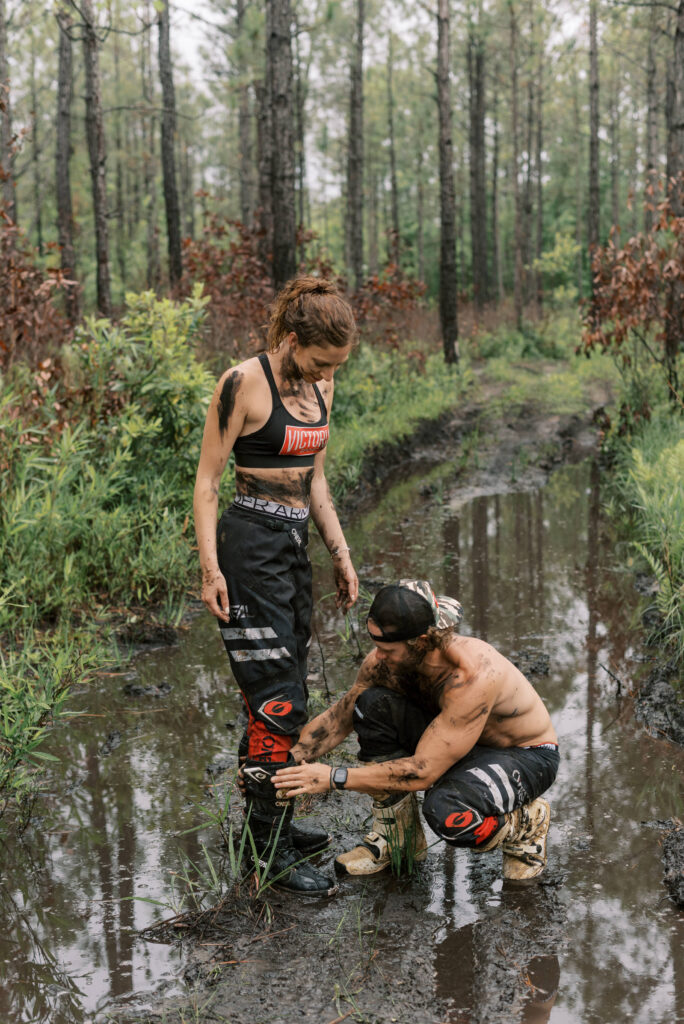 man fixes his girlfriend's boot during their dirt bike photoshoot